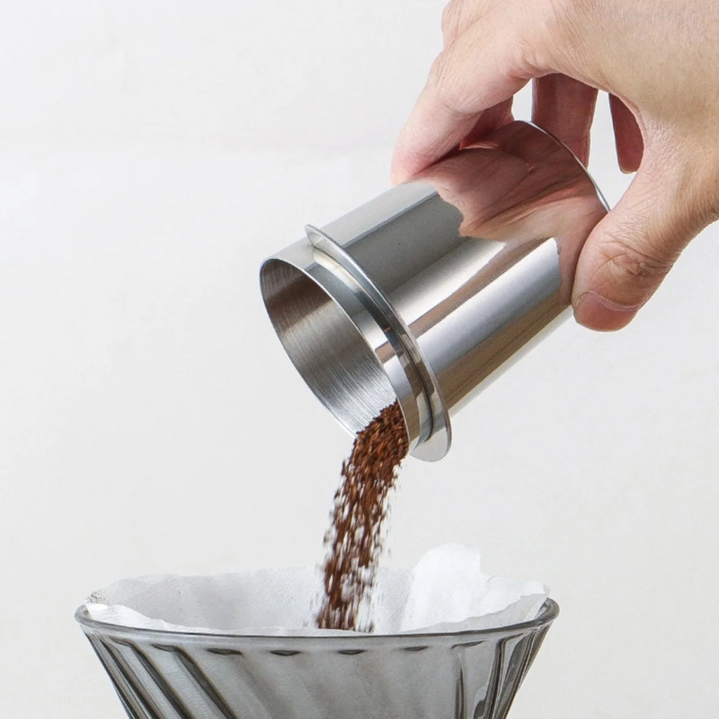 Pouring ground coffee from the stainless dosing cup into a pour-over dripper