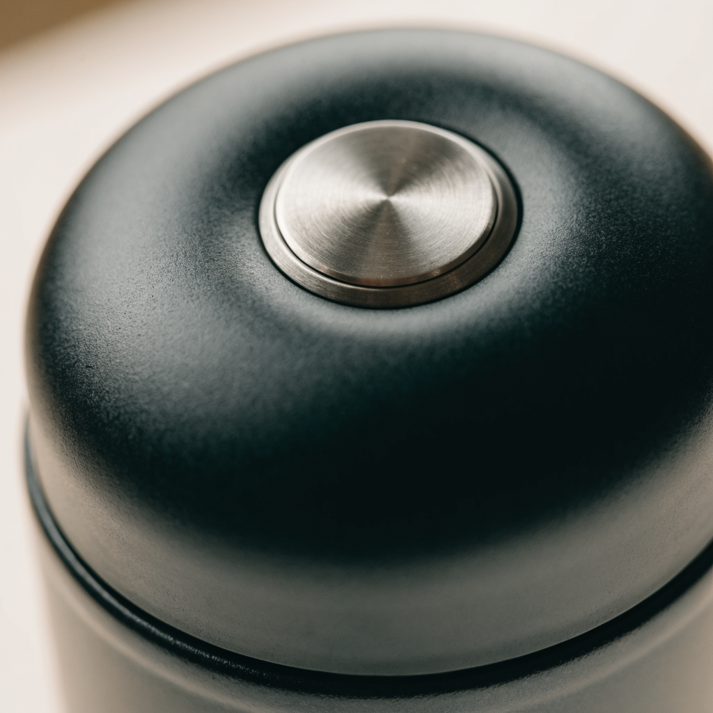 Close-up of the matte black dome lid and brushed-silver press button of the vacuum coffee canister