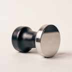Espresso tamper lying on its side, showing the flat mirror-polished face of the stainless steel base