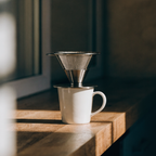 Stainless mesh pour-over dripper brewing over a white mug on a wooden counter